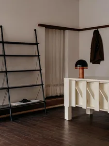 A minimalist interior design featuring a black metal shelving unit and a white wooden console table with a black lamp on top.