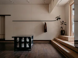 A modern entryway featuring a minimalistic design with concrete walls and flooring, a sleek black desk, and a potted plant on
