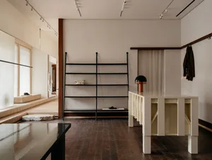 A modern retail space featuring black metal shelves, a white table, and a mix of materials including wood, fabric, and stone.