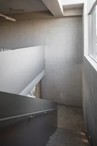 A minimalist concrete stairwell with a white railing and a window on the right side.