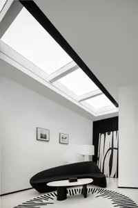 A minimalist living room with black and white decor and light streaming in from skylights.
