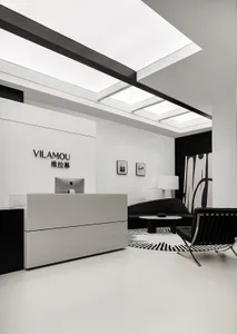 A minimalist modern office lobby with a sleek white desk, black seating, and skylights.