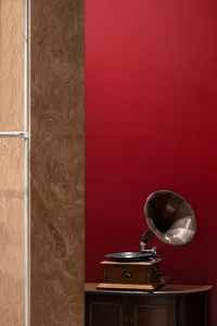 A vintage Victrola record player with a wooden cabinet and a large metal horn speaker against a red wall, placed on a wooden 