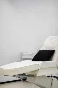 A white medical spa chair with a black pillow on a white floor in a minimalist design.