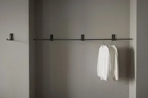 Black metal clothing hanger with two white shirts hanging on a minimalist, industrial-style wall-mounted system in a monochro