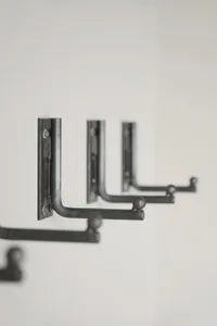Three metal hooks mounted on a white wall, featuring a modern industrial design.
