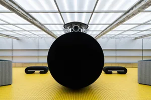 A minimalist installation featuring a black sphere in an industrial setting with an industrial-style ceiling