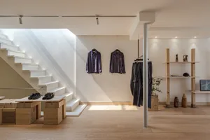 A minimalist retail store with neutral materials, featuring a display area with clothing hanging on the wall and shoes on the