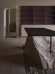 A modern bench featuring a unique design with a rock base, placed in a minimalist space with a concrete wall and floor.