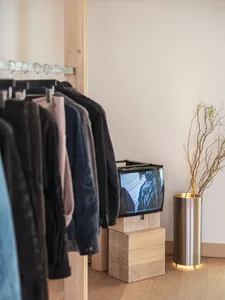 A modern clothing retail store display featuring a wooden cabinet with a flat-screen TV and a metal and branch lamp on a wood