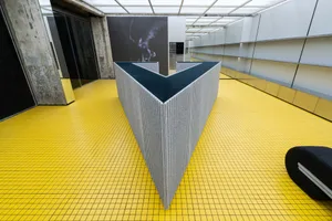 An industrial-style lobby featuring a modern concrete structure with a yellow tiled floor.