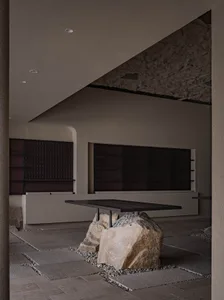 A minimalist interior space featuring a concrete table surrounded by large rocks, with dark walls and a low ceiling.