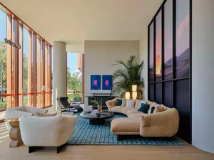 A modern minimalist living room with a plush fabric couch, two plush white armchairs, and a wooden coffee table on a blue rug