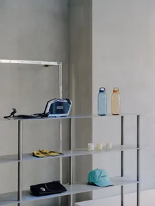 Minimalist metal shelves displaying various products, including a blue bag, colorful bottles, a yellow scarf, and a teal hat.