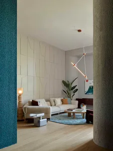 A modern living room featuring a circular wooden table on a wooden floor, surrounded by contemporary furniture and plants.