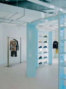 Retail interior displaying clothing on shelves with glass columns and metal railings.