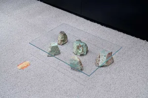 A glass table with green rocks on it, placed on a carpeted floor.
