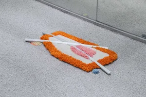 A decorative textile object with white, blue, and orange hues lying on a carpeted floor.