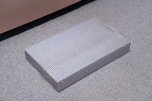 A concrete block with horizontal grooves and circular indentations on a gray carpeted floor.