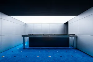 An empty reception desk with a minimalist design, featuring sleek metal surfaces and a clear glass top, illuminated by bright