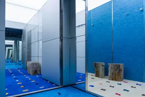 A minimalistic playroom with blue carpet, wooden stools, and glass panel walls.