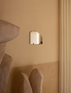 A minimalist, geometric mirror with the word 'truth' on a metallic surface, mounted on a beige wall.