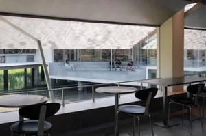 A modern cafe with tables hanging from a cantilevered structure, featuring steel frames and glass tops, with a glass wall and