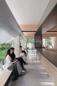 People sitting on benches in a modern glass-walled interior space.