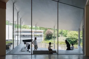 People in a modern, minimalist space with large glass windows overlooking a natural landscape.