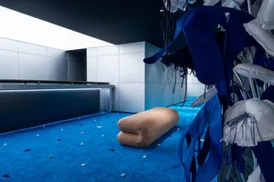 A modern interior space with a blue carpet, a beige cylindrical object, and hanging fabric elements.