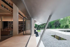 A modern library with concrete walls and a glass door overlooking a water body and greenery.