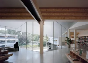 People reading in a minimalist library with large windows and a concrete floor.