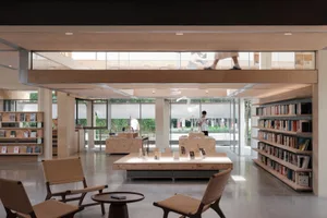 A spacious modern library interior with natural lighting, wooden shelves, and minimalist furniture.