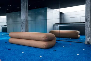 Two modern beige lounge sofas on a blue carpet in a contemporary interior space.