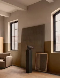 A modern interior space with warm neutral tones, featuring a minimalist couch, a large window, and contemporary decor element