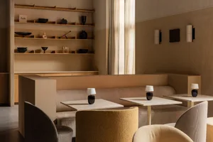 A minimalist restaurant interior featuring marble tables, fabric chairs, and wooden accents.