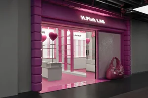 A storefront with pink acrylic elements including a large pink bag, heart-shaped balloons, and a pink floor.