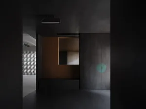 A minimalist corridor with concrete walls and floor, featuring a circular light fixture and a wooden panel with a geometric p