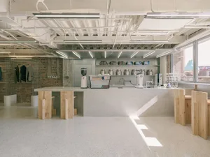 A modern industrial coffee shop kitchen with concrete countertops and exposed pipes.
