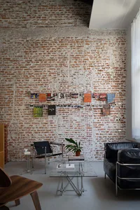An industrial living room featuring brick and concrete walls, a glass coffee table, and a black leather armchair.
