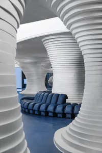 A modern industrial lobby with blue sofas and white concrete columns and ceiling.