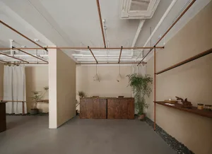 Intimate minimalist commercial space with concrete walls and floor, industrial-style lighting, and simple furniture.
