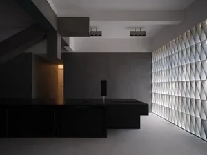 A modern interior design featuring concrete walls and a minimalist kitchen with a black countertop.