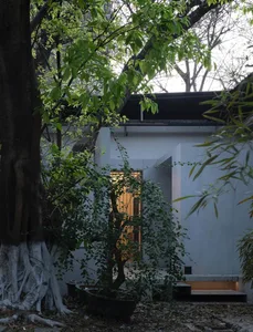 A modern exterior building with concrete walls and a glass door, surrounded by greenery.