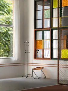 A modern interior with a window featuring colorful panes, a metal stool, and a sleek coat rack.
