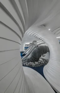 A white, spiral indoor space with a black, futuristic sculpture resembling a tornado in the center.