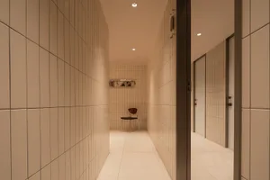 A minimalist corridor with tiled walls and a single chair in the distance.
