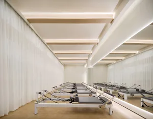 A minimalist fitness center with curtained walls and Pilates reformers lined up in rows.
