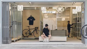 A modern retail storefront with glass walls showcasing a selection of clothing and a bicycle parked inside.