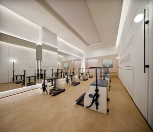 A minimalist fitness studio with hardwood floors features modern Pilates Reformers and mirrors.